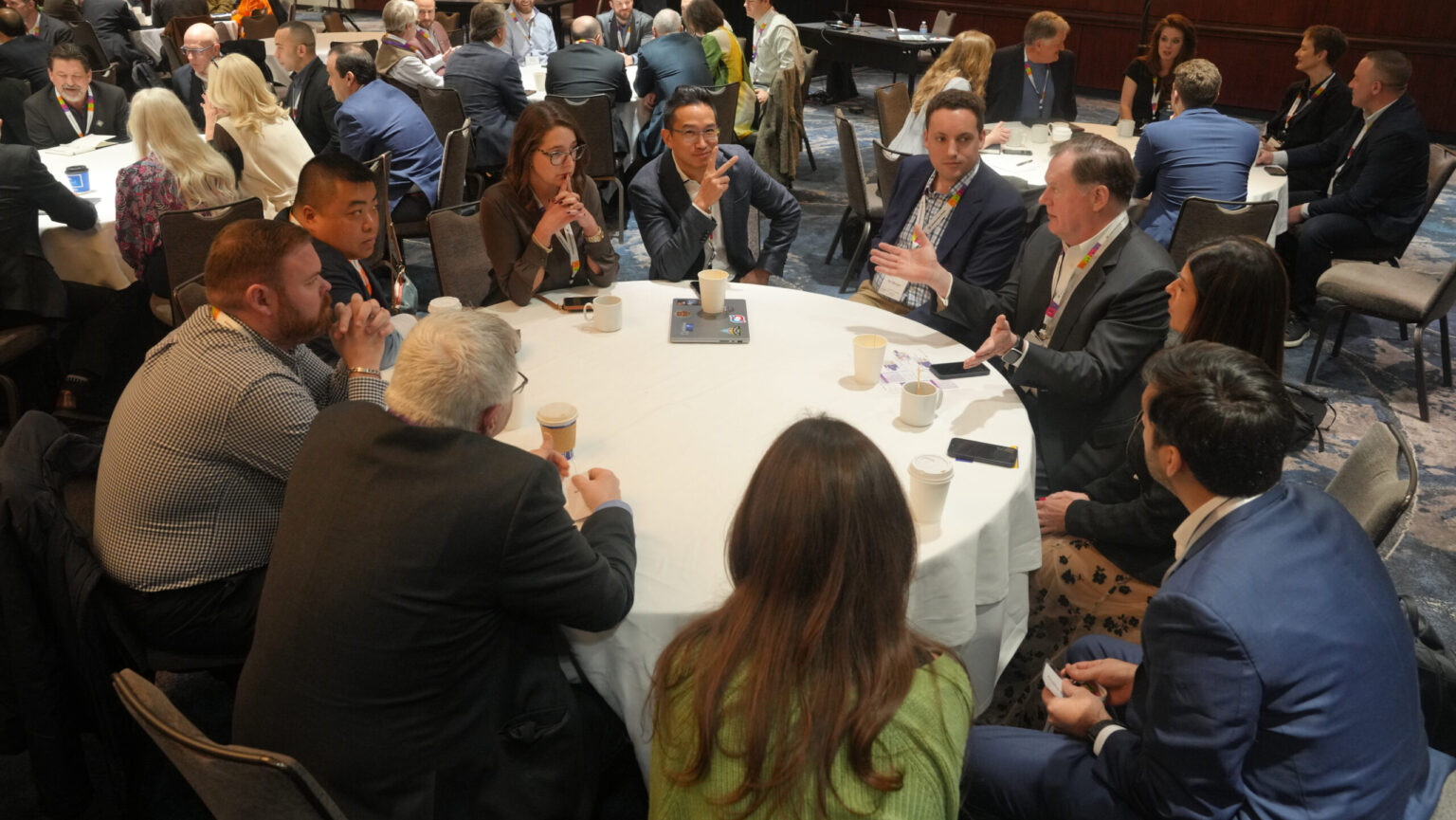 12 members of the industry sit and discuss around a round white table.